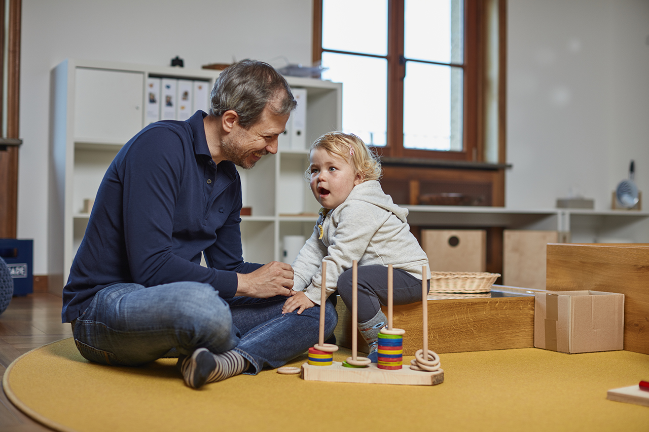 Ein Vater, der mit seinem Kind auf dem Boden mit Holzsspielzeug spielt.